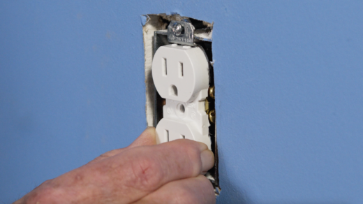 a hand holding a loose electrical outlet in the blue-colored wall