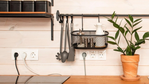 A modern kitchen setup with multiple electrical outlets on a wooden wall, surrounded by hanging kitchen utensils and a potted plant