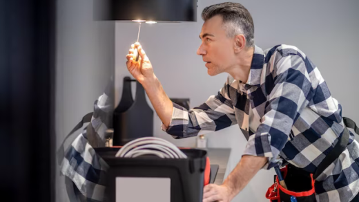 Focused man touching a lamp on a kitchen hood with a screwdriver